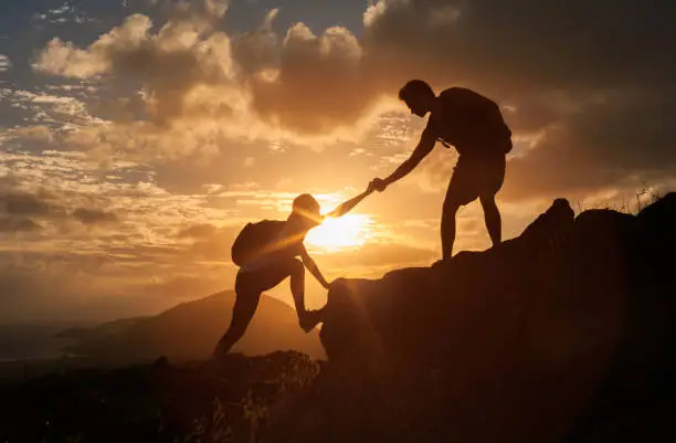 Male and female hikers climbing up mountain cliff and one of them giving helping hand.  People helping and team work concept.