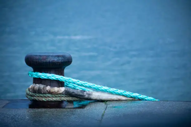 Photo of Harbor mooring post, thick ropes, sea background.
