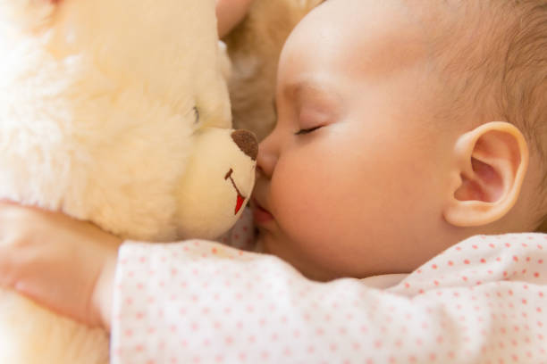 Little baby girl sleeping in a white bed with a soft bear, healthy baby sleep
