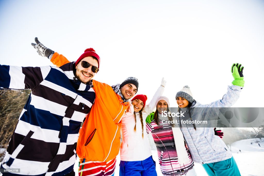 Young friends in ski-wear with arms raised Young friends in ski-wear with arms raised on winter holiday. 20-29 Years Stock Photo