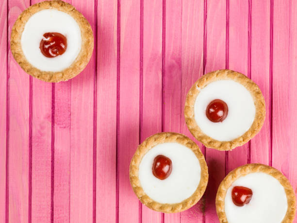 Iced Bakewell Tarts With a Cherry Individual Iced Bakewell Tarts On A Pink Background bakewell stock pictures, royalty-free photos & images