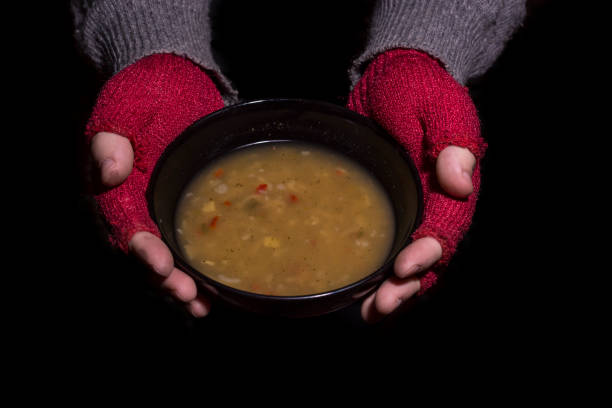 Poverty concept. Man with red gloves holding a bowl of soup isolated on black background.