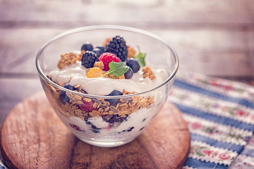 Granola with yogurt and berries on a dark brown background. Healthy breakfast with yogurt, baked granola, blueberries and raspberries. Top view. Copy space