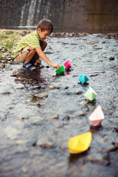 istock Little boy playing paper boats in stream 641389908