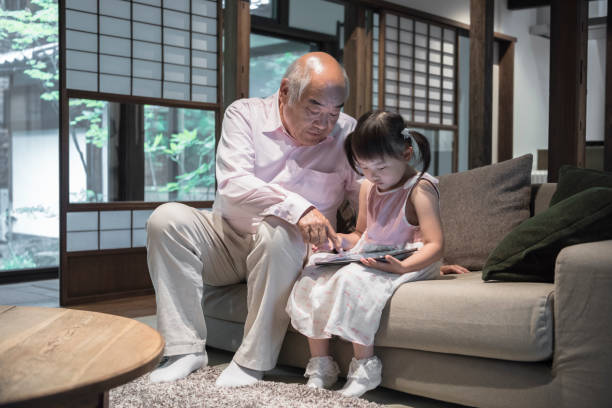 grand-père avec petite fille sur le canapé à l’aide de tablette numérique - japan serious family senior adult photos et images de collection