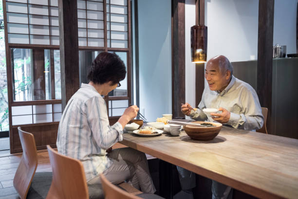 Japanese couple enjoying meal together at home Senior Japanese man and mature woman sitting at table eating food, candid view of two Japanese people eating dinner only japanese stock pictures, royalty-free photos & images