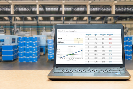 Laptop with analysis screen on table with blur warehouse cargo in factory. Smart factory concept.
