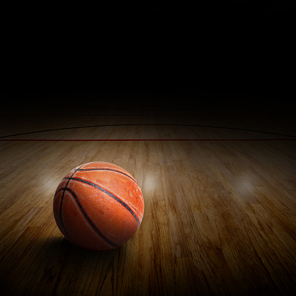 Dramatic spot lighting on basketball arena with ball on court and copy space.