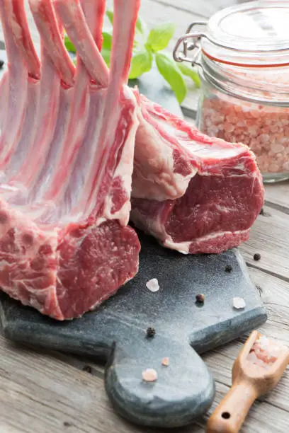 Raw uncured lamb ribs with basil and pink salt on the stone cutting board on the wooden background