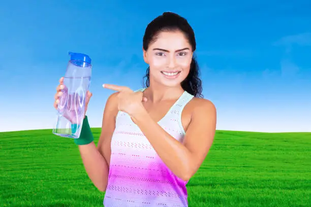 Portrait of beautiful woman holding and pointing a bottle while standing in the meadow