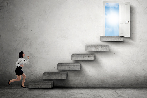 Young businesswoman running through a staircase toward an opportunity door to success