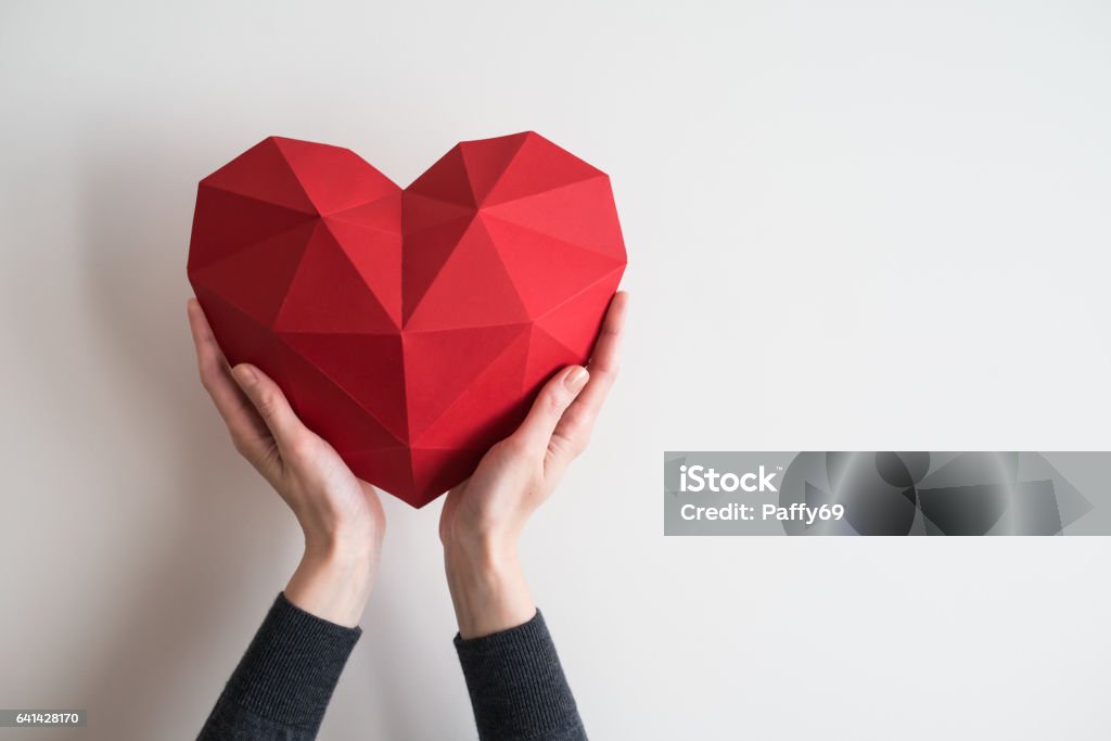 Manos femeninas sosteniendo la forma de corazón poligonal rojo - Foto de stock de Símbolo en forma de corazón libre de derechos