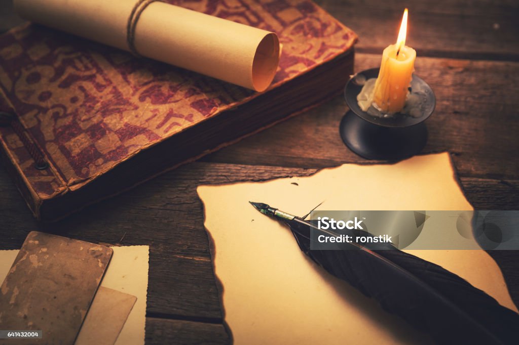 vintage feather with paper and old book on table vintage feather with paper and old book on table in light of candle Antique Stock Photo
