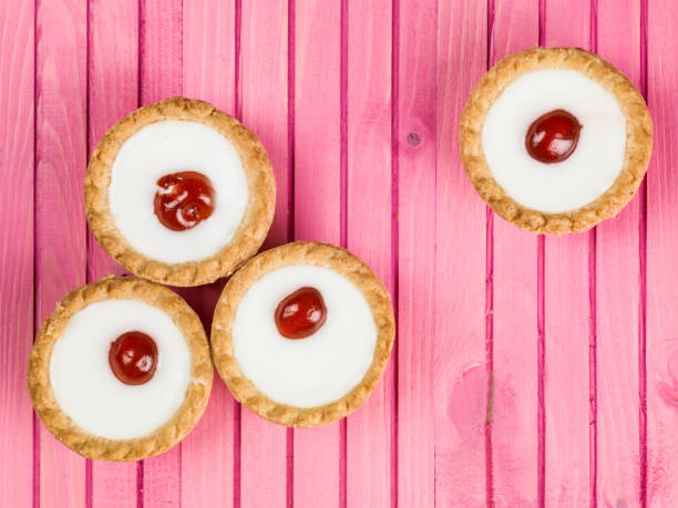 Bakewell Tarts On A Pink Background Individual Iced Bakewell Tarts On A Pink Background bakewell stock pictures, royalty-free photos & images