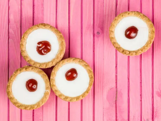 Individual Iced Bakewell Tarts On A Pink Background