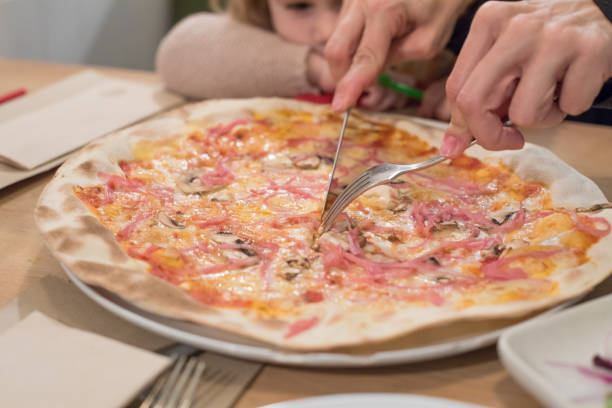 istock child looking mother hands cutting pizza with fork and knife 641447774