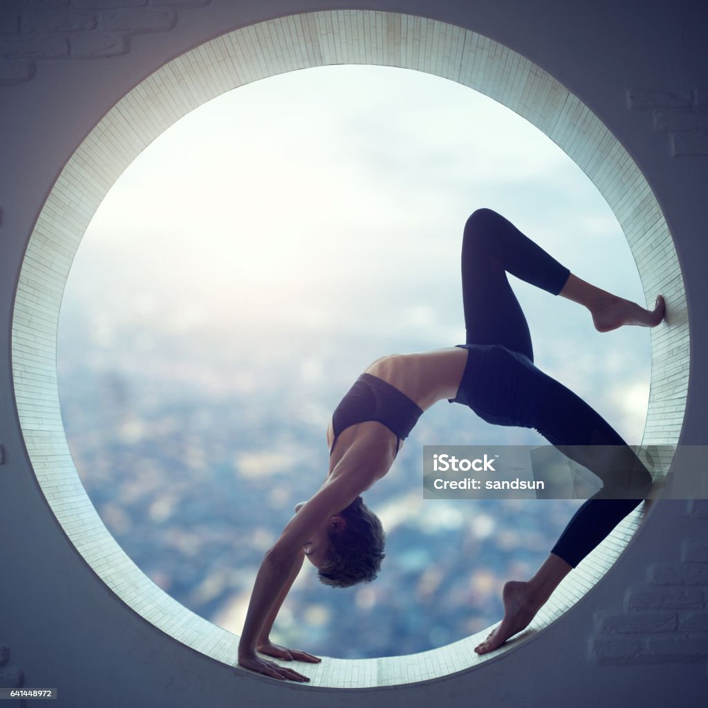 Young woman doing yoga Young woman doing yoga in the round window Flexibility Stock Photo