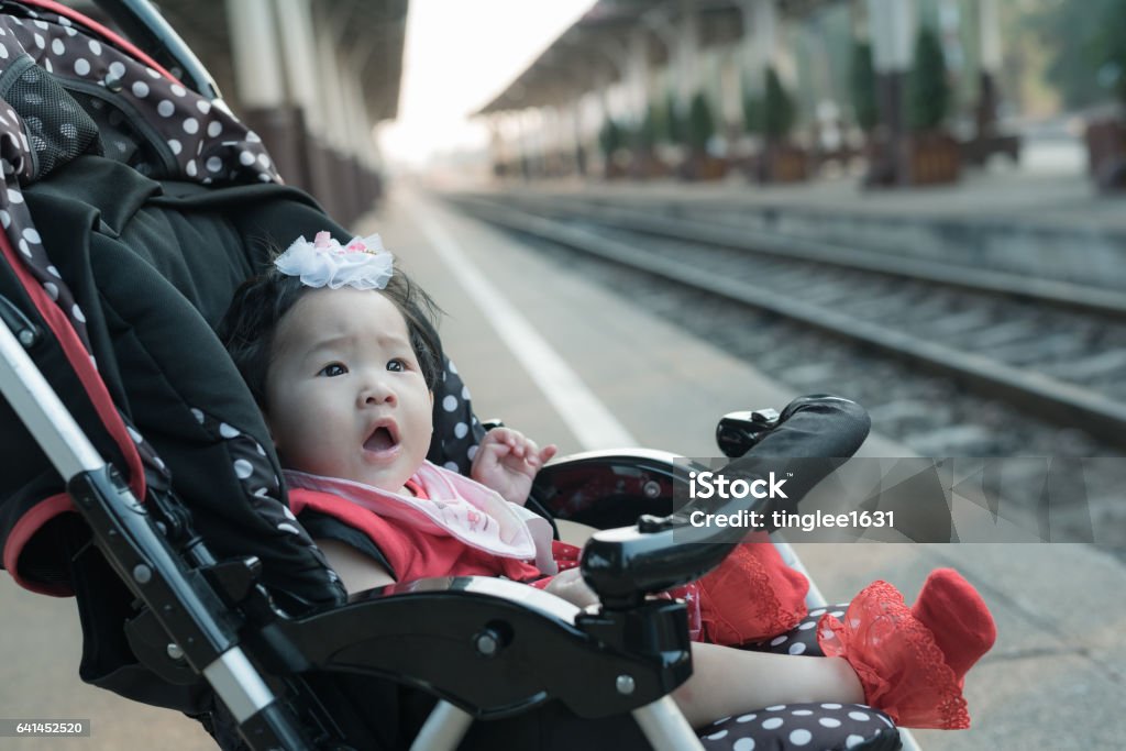 Asian baby girl sitting in stroller in railway station. Adorable asian baby girl sitting in stroller on a walk in railway station. Baby Carriage Stock Photo