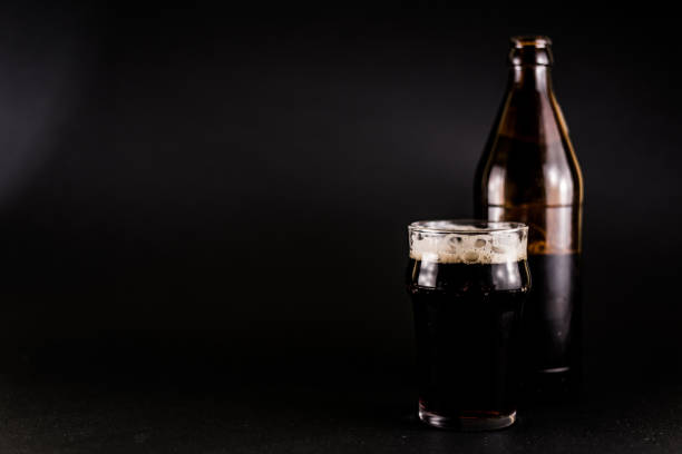 Dark beer and bottle on black background, copy space