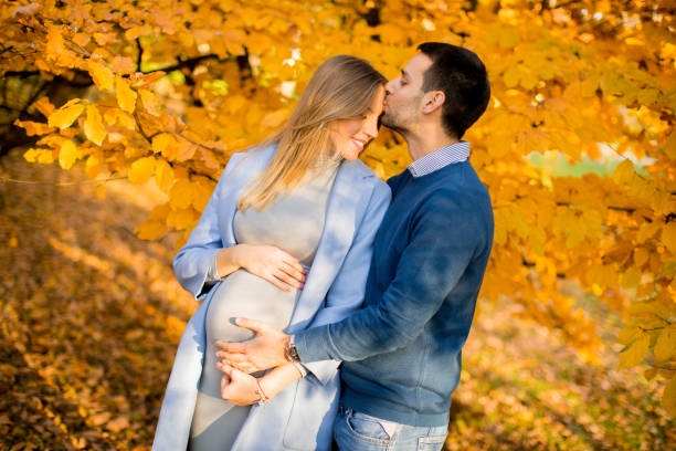 View at pregnant woman and man posing at autumn park