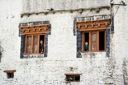 Mother and son looking through the window nearby Skiu village. Traditional house with whitewashed walls and carved wooden windows.