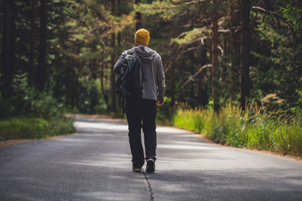 Backpacker walking alone by the road through the forest.