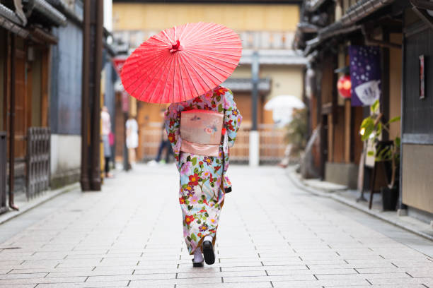 Following Tradition and my Cultures Japanese woman walking with traditonal umbrella in the traditional part of Kyoto. kimino stock pictures, royalty-free photos & images