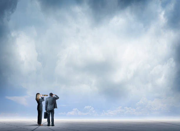 A businesswoman looks through a spyglass as she stands next to a businessman who places his hand above his brow as they both look into the distance as they stand on a generic map that spans the ground they stand on.  A stormy an ominous sky hovers above them.