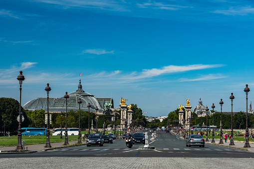 Cars and tourists on the Alexandre III bridge, known for its golden statues, with view of the big palace in the background.