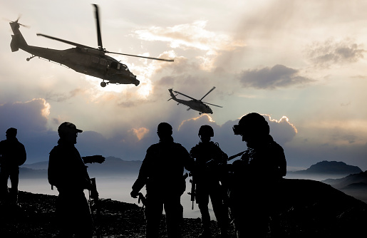 Silhouette of soldiers and helicopters during a military mission at dusk.
