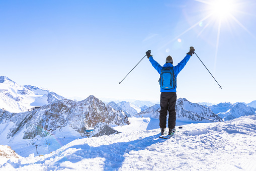 Back view of a happy skier with raised hands as a symbol of victory looking at a panoramic view of the snow white mountain landscape around