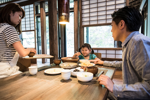 Japanese parents with young girl sitting at table eating meal, food on table