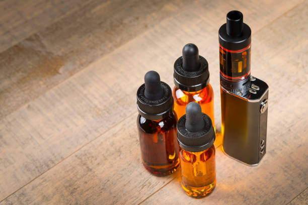 istock Vaping mod e-cig with tank atomizer and juice bottles over wood background 641509478