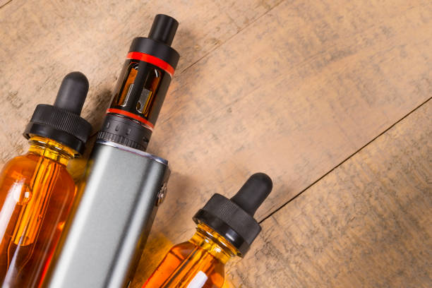 istock Vaping mod e-cig with tank atomizer and juice bottles over wood background 641509536
