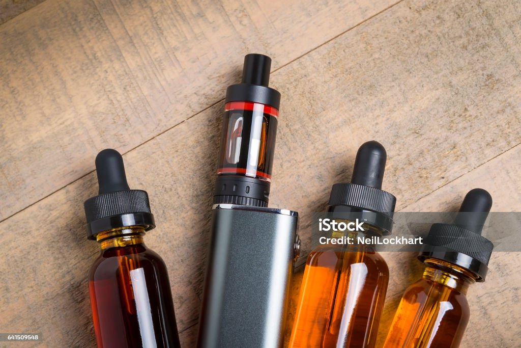 Vaping mod e-cig with tank atomizer and juice bottles over wood background Electronic Cigarette Stock Photo