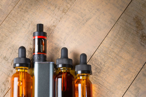 Vaping mod e-cig with tank atomizer and juice bottles over wood background