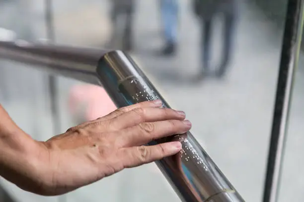Hand reading Braille inscriptions for the blind on public amenity railing