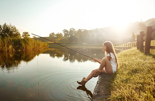 side view of young woman fishing in summer day, enjoying outdoor activity and relaxing.photo taken at the edge of lake.