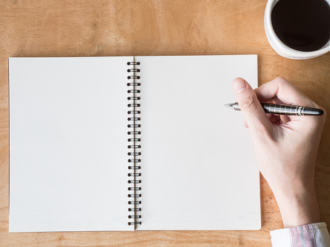 Man hands with pen writing on empty notepad over wooden table.