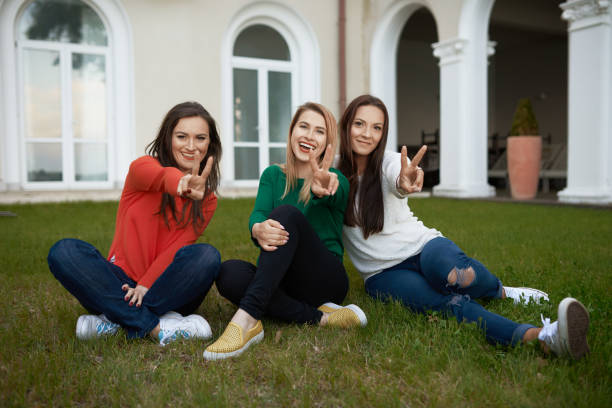 happy tree friends enjoying their spring day on the grass, side by side, showing peace sign. casual wear.