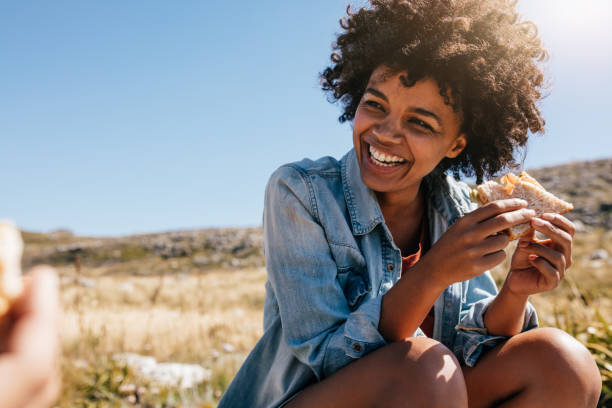 Happy young woman taking break during country hike. Happy young african woman eating sandwich and smiling. Taking break during country hike. sandwich stock pictures, royalty-free photos & images
