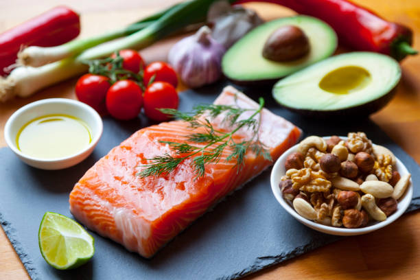 Foods Items High in Healthy Omega-3 Fats. Table top still life of foods high in healthy fats such as Salmon, olive oil, nuts and avocados with vegetables and herbs. atkins diet stock pictures, royalty-free photos & images