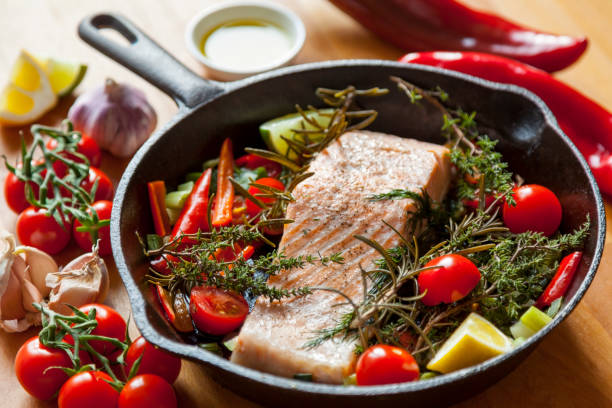 Pan Seared Salmon Steak in Steel Skillet with Fresh Vegetables Pan seared salmon steak with fresh herbs, tomatoes, red peppers, shallots, garlic, lemon and olive oil in a steel skillet. paleo diet stock pictures, royalty-free photos & images