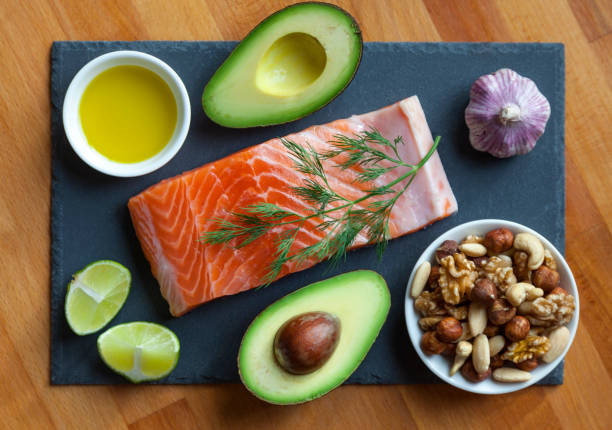 Healthy Fat Foods Table top still life of foods high in healthy fats such as olive oil, Salmon, nuts and avocados with vegetables and herbs. paleo diet stock pictures, royalty-free photos & images