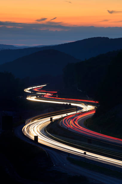 夕暮れの丘を介して蛇行高速道路の車の長時間露光が点灯します。 - curve road winding road street ストックフォトと画像