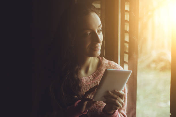 istock Thoughtful young woman holding digital tablet by window 641567952