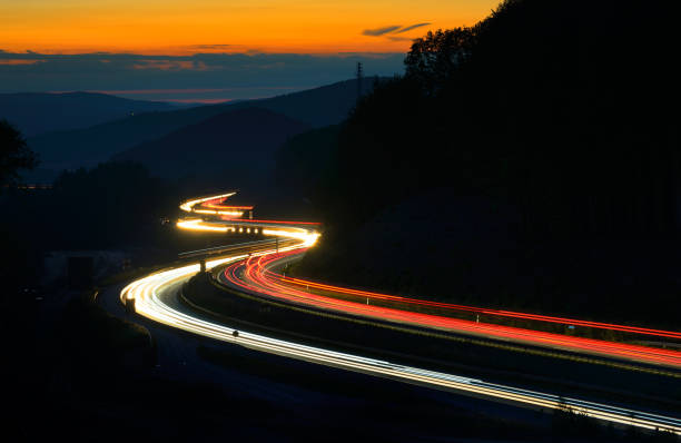 długa ekspozycja świateł samochodowych na autostradzie meandering przez wzgórza o zachodzie słońca - road winding road highway mountain zdjęcia i obrazy z banku zdjęć