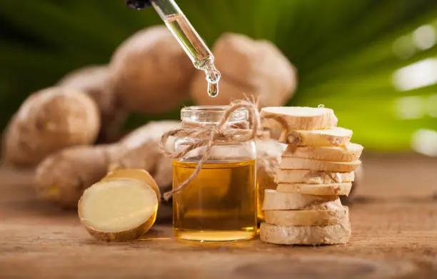 Oil of ginger in a small glass bottle macro and root on tropical leaves background