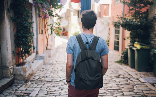 Young tourist man with backpack is walking through the streets of Rovinj in Istria, Croatia, Southeastern Europe. He is enjoying a nice summertime day, relaxing in the old coastal town.
