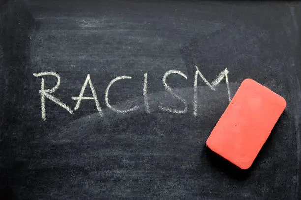 Photo of erasing racism, hand written word on blackboard being erased concept